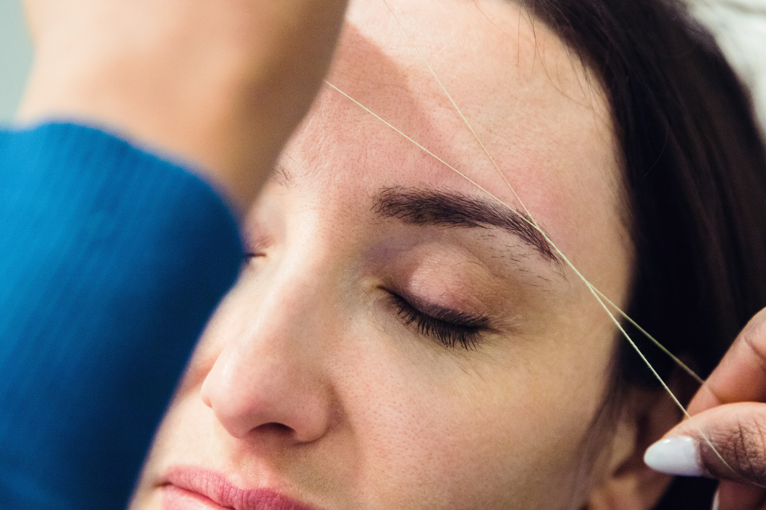 Caucasian woman removing hair from eyebrows with thread technique done by eyebrow stylist. Threading. Process Steps. Close up